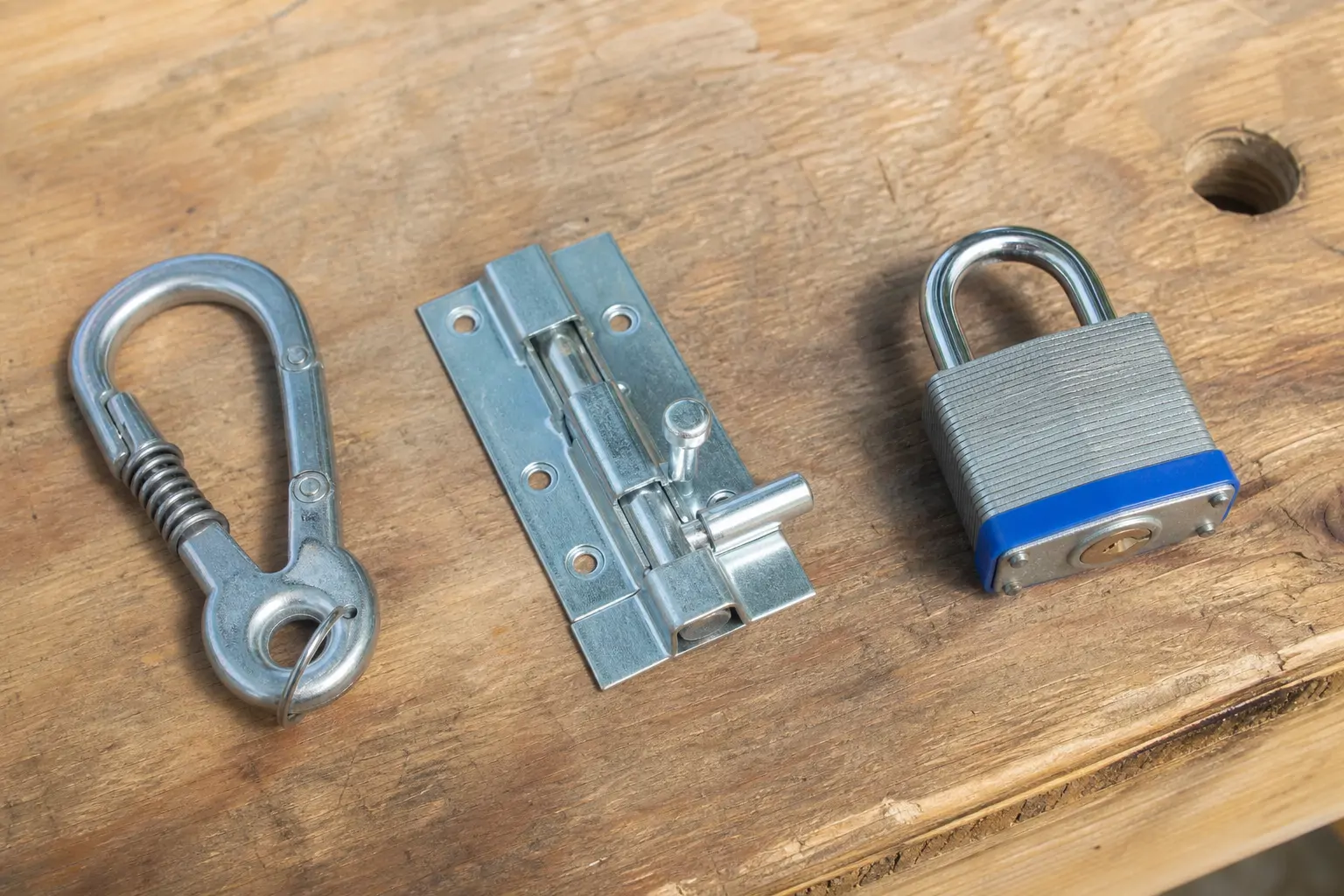 Three different coop door lock types laid side by side on a wooden surface for comparison